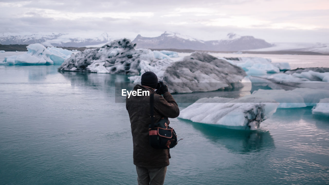 Man photographing with camera in winter against sky