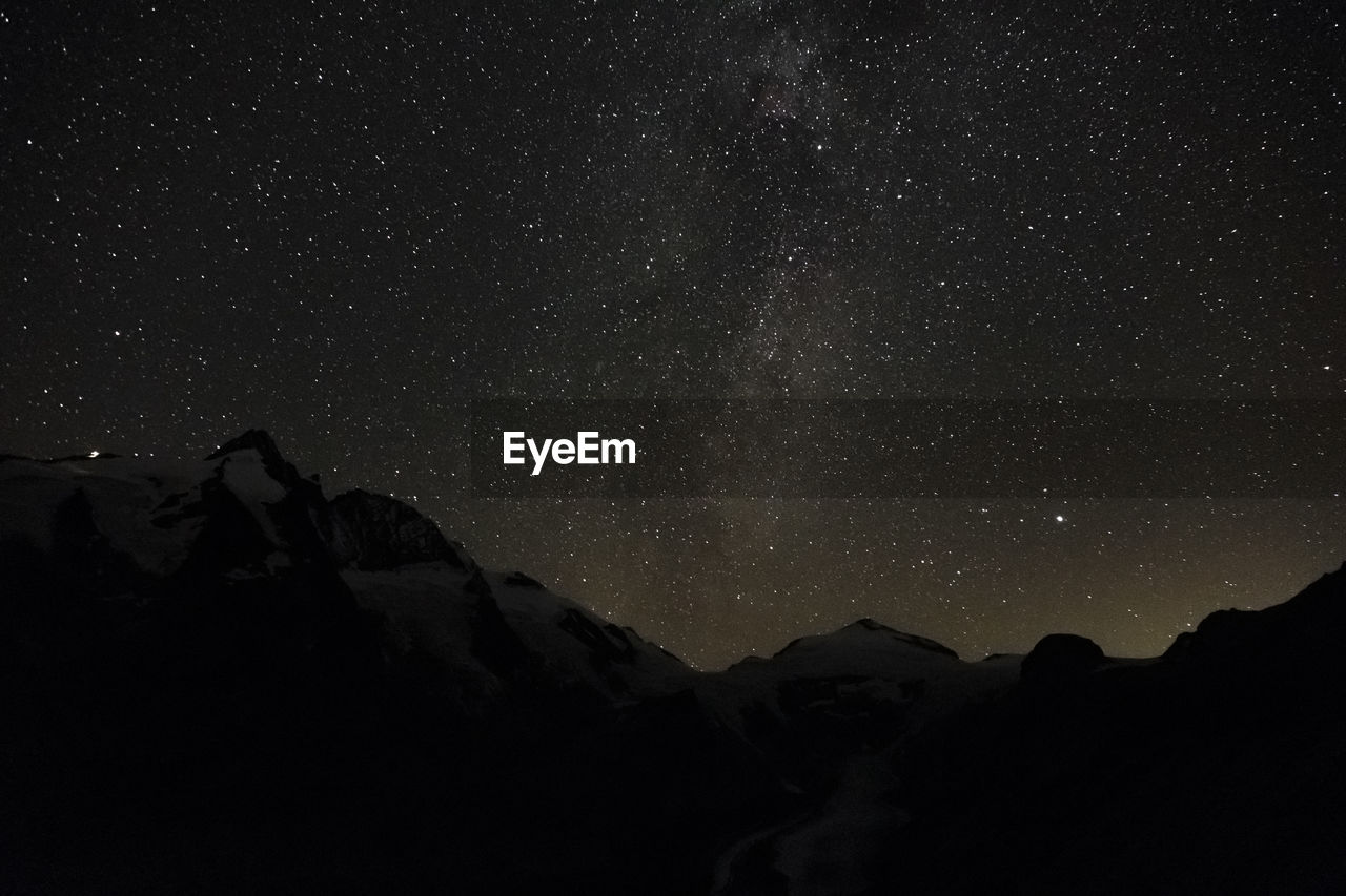 LOW ANGLE VIEW OF SILHOUETTE MOUNTAIN AGAINST STAR FIELD