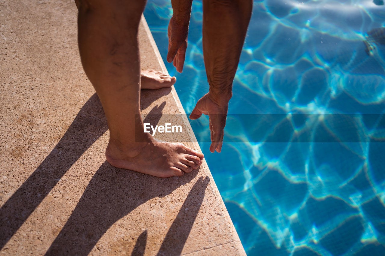 High angle of crop anonymous barefoot person stretching forward while standing on poolside edge near clean water person