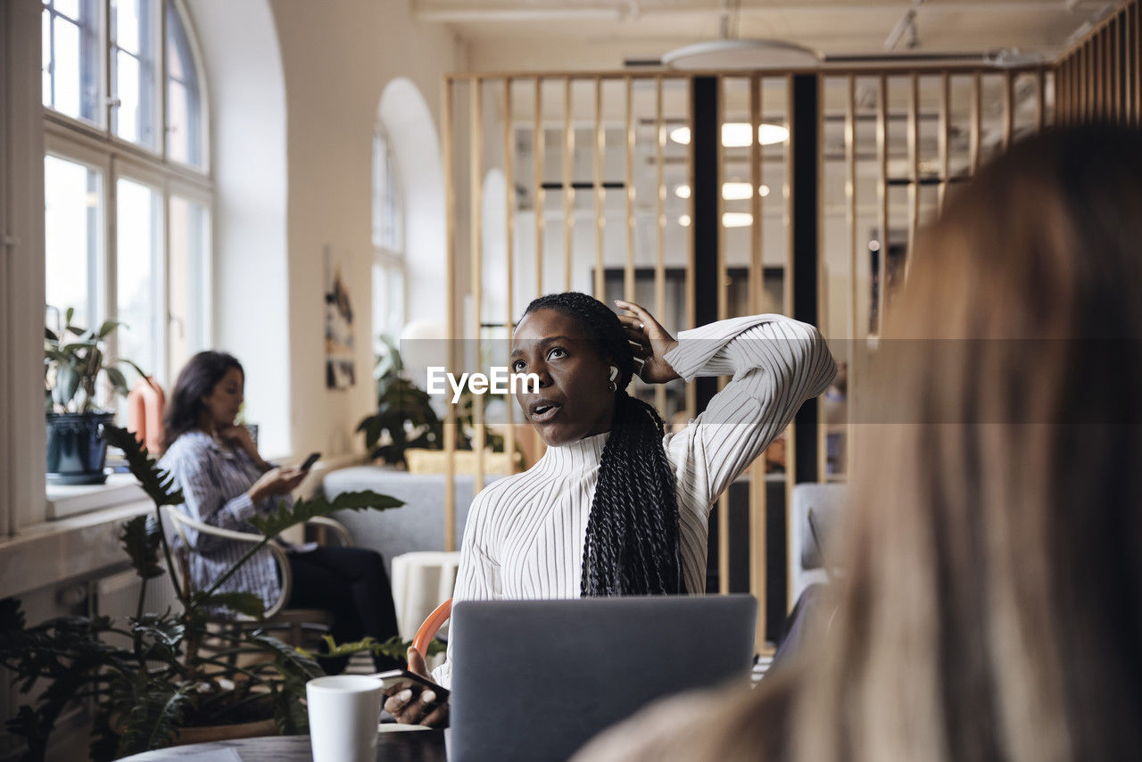 Businesswoman looking up while talking through wireless in-ear headphones at coworking office