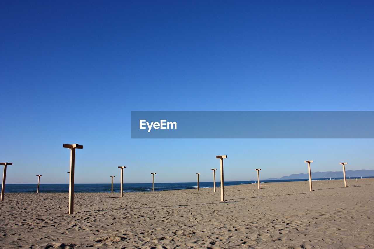 WOODEN POSTS AT BEACH AGAINST CLEAR BLUE SKY