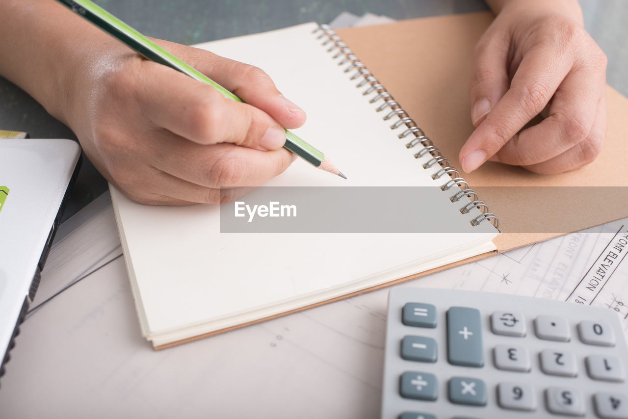 Cropped hands of woman writing on book at desk