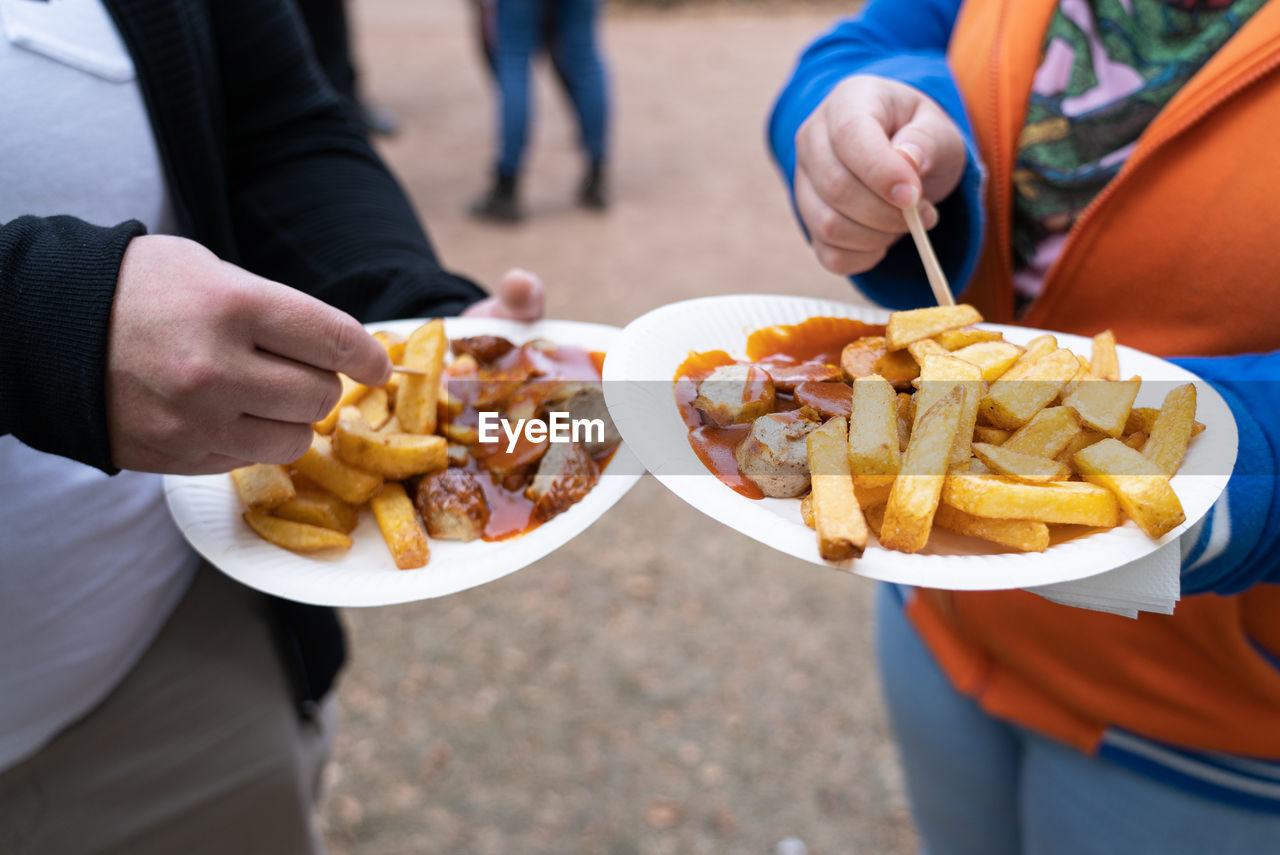 Couple with two paper plates with french fries and currywurst