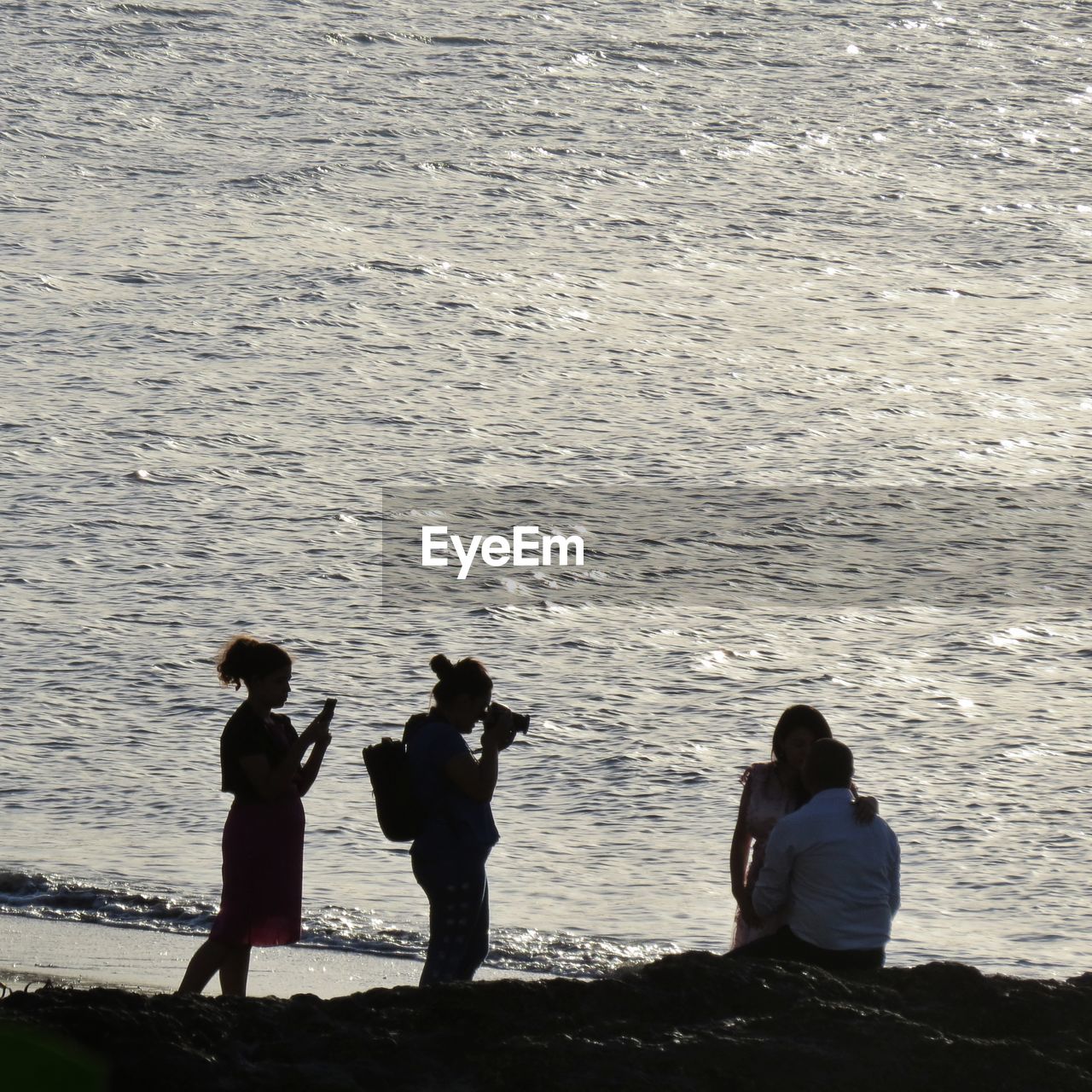 REAR VIEW OF PEOPLE STANDING AT BEACH AGAINST SKY