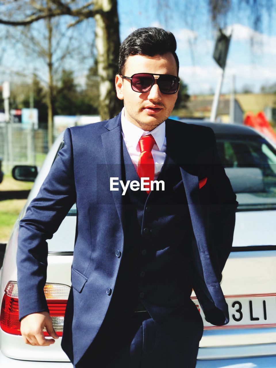 Young businessman wearing sunglasses while walking by car