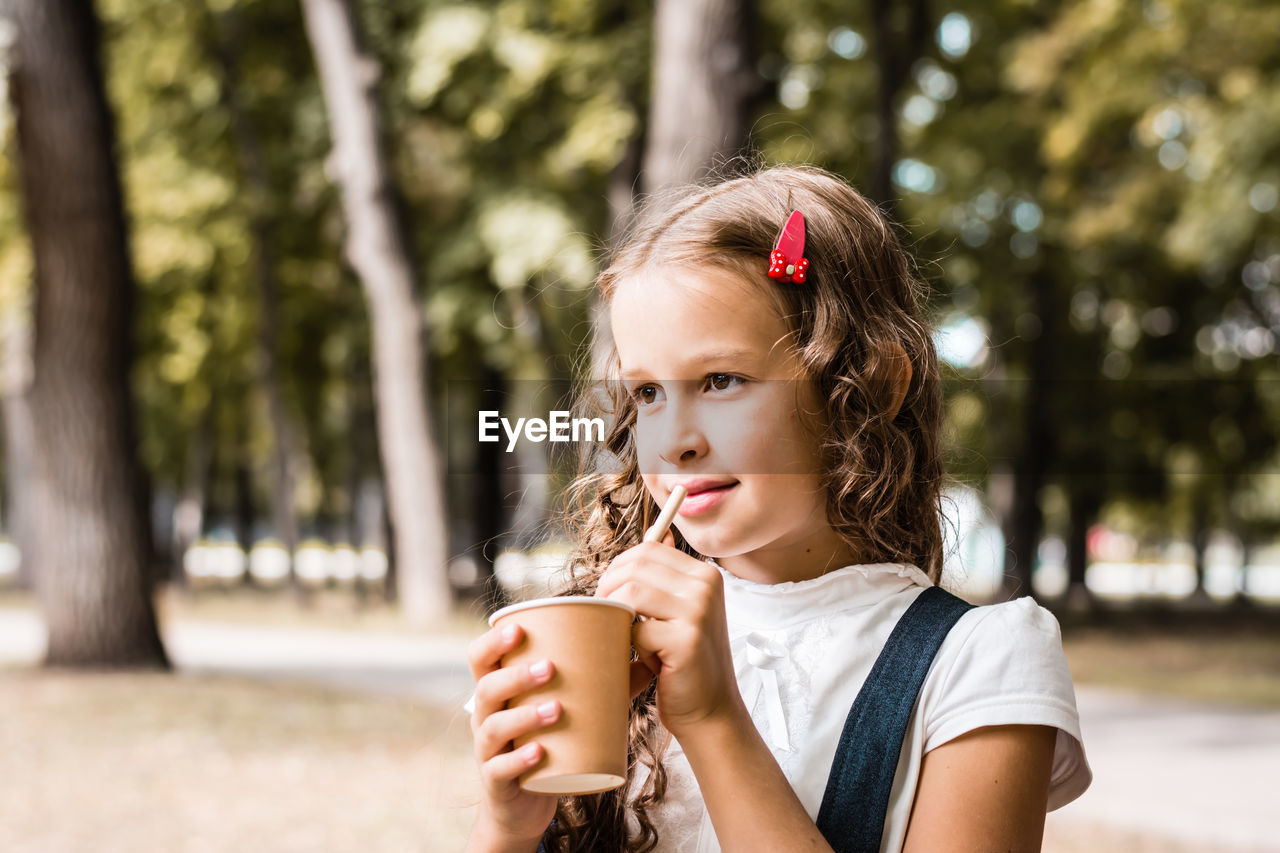 Schoolgirl drinking from an eco-friendly cup and straw in the park
