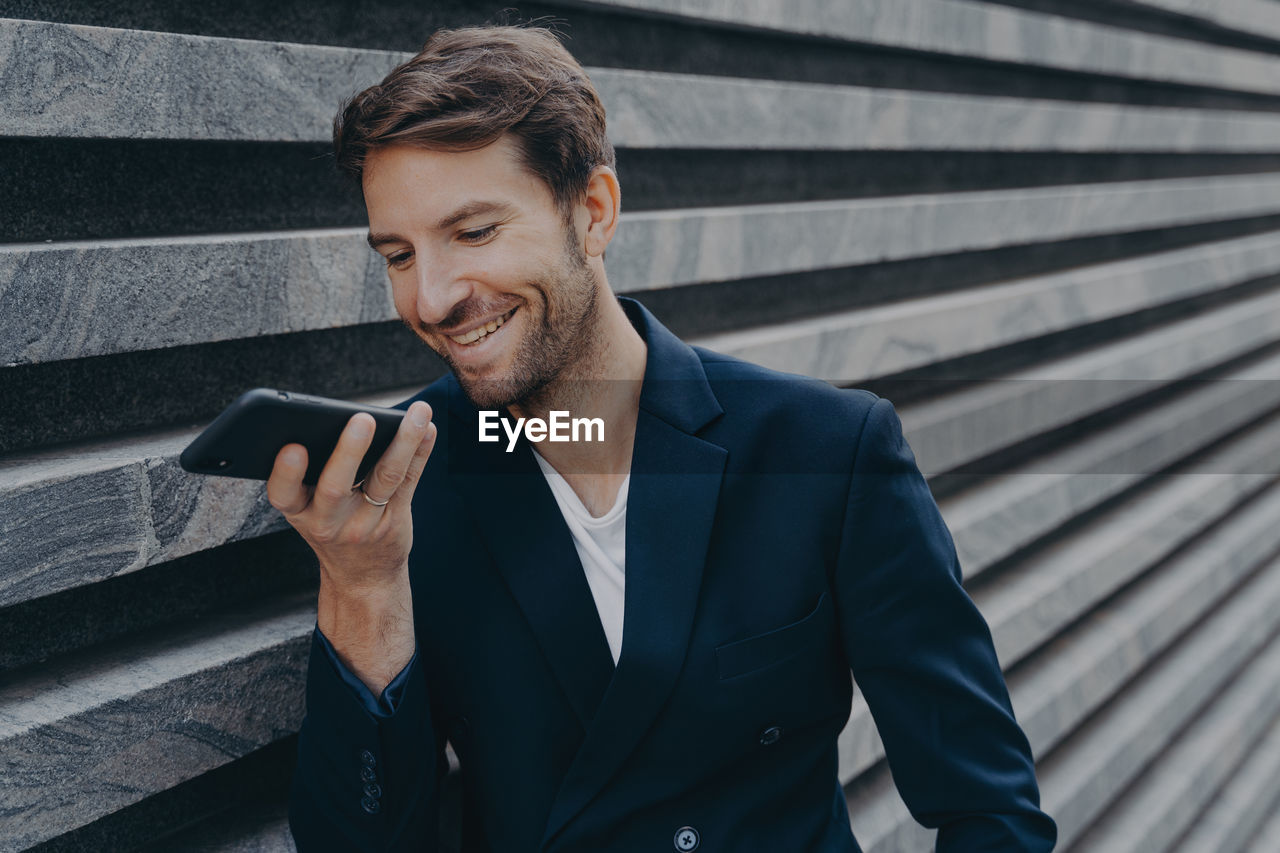 YOUNG MAN USING MOBILE PHONE WHILE STANDING ON LAPTOP