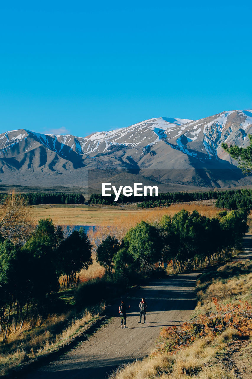 Men standing on road amidst trees against mountains during winter