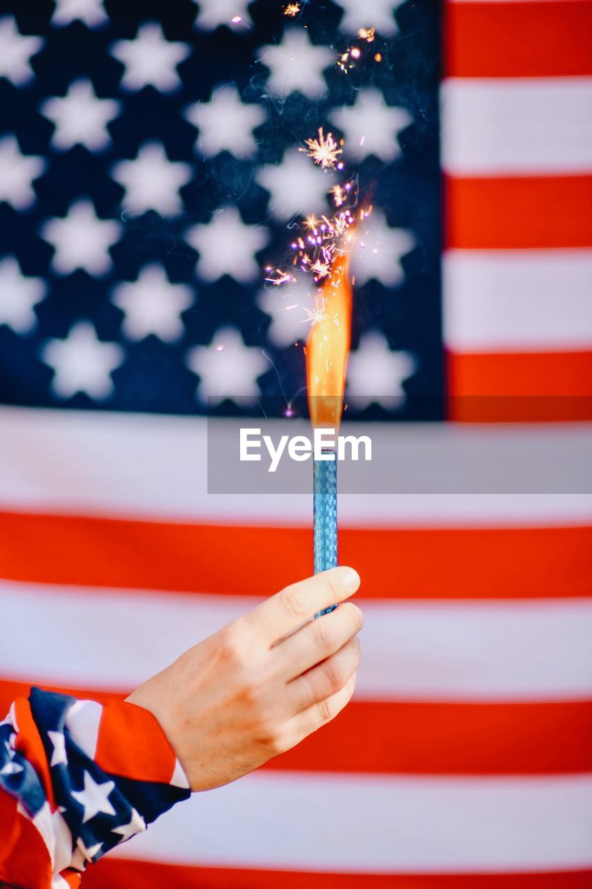 Cropped hand holding lit firework against american flag