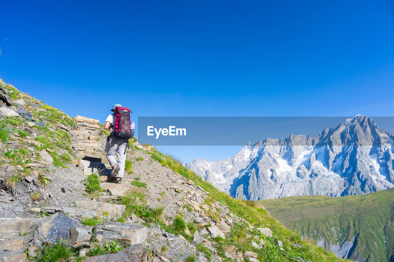 Rear view of hiker walking on mountain against clear blue sky