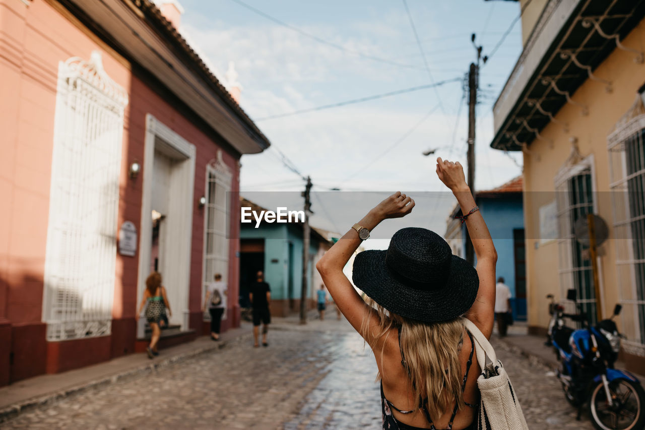 Rear view of young woman wearing hat while standing on city street against sky