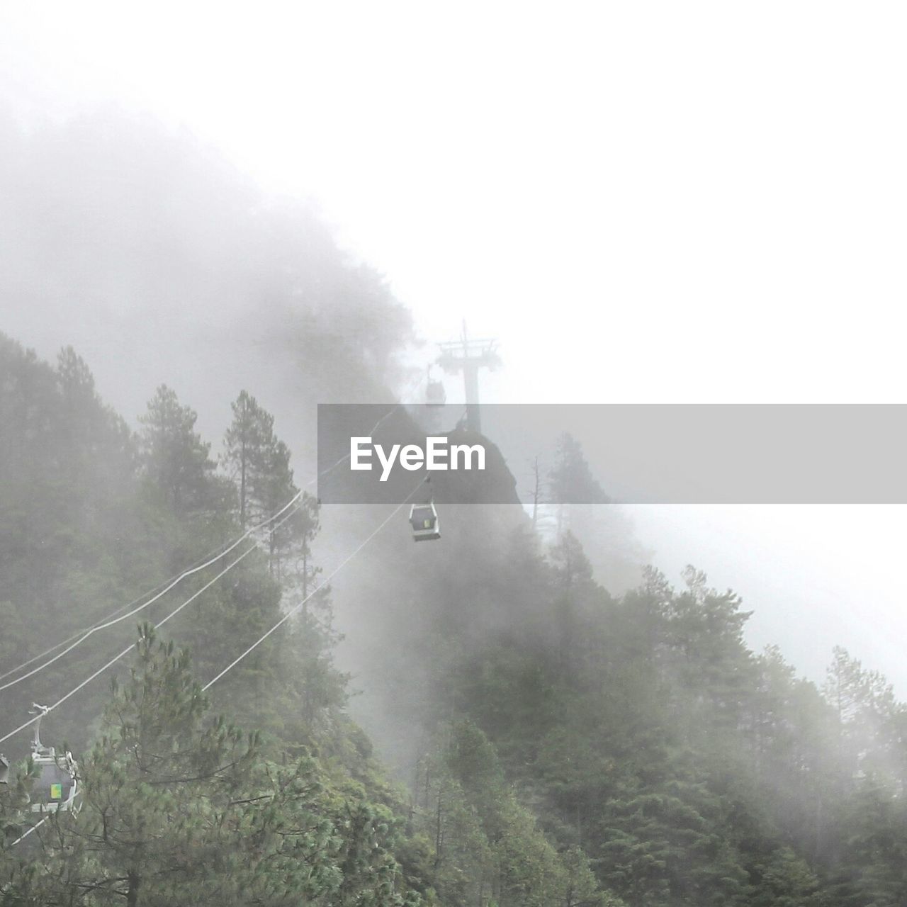 Overhead cable cars leading towards mountain during foggy weather