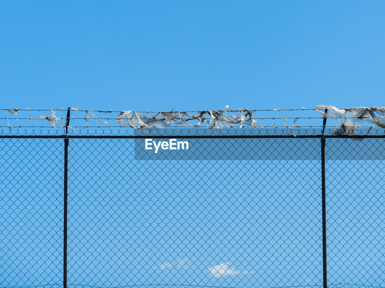 Low angle view of chainlink fence against clear blue sky