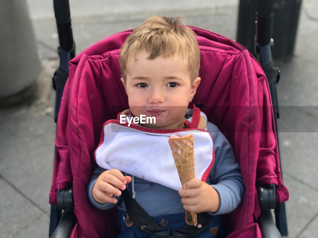 Portrait of cute baby boy eating ice cream while sitting on stroller