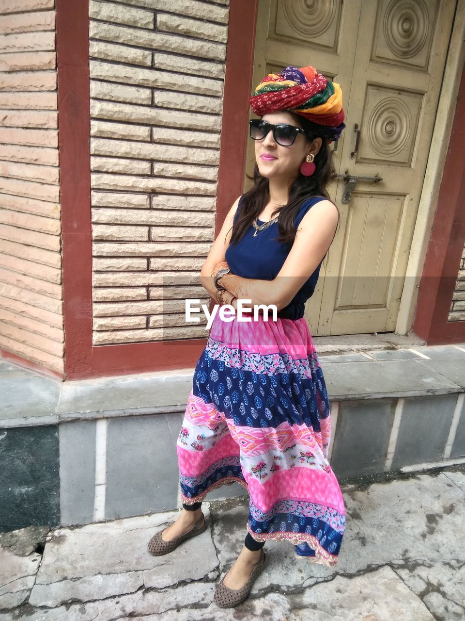 Portrait of young woman wearing turban and sunglasses against house