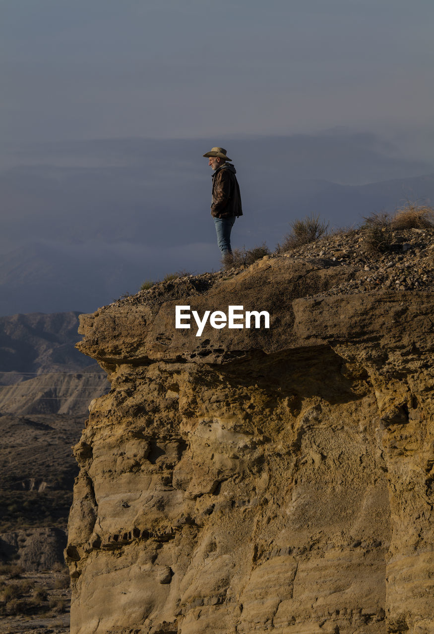 Adult man in cowboy hat standing on top of cliff in tabernas desert, almeria, spain