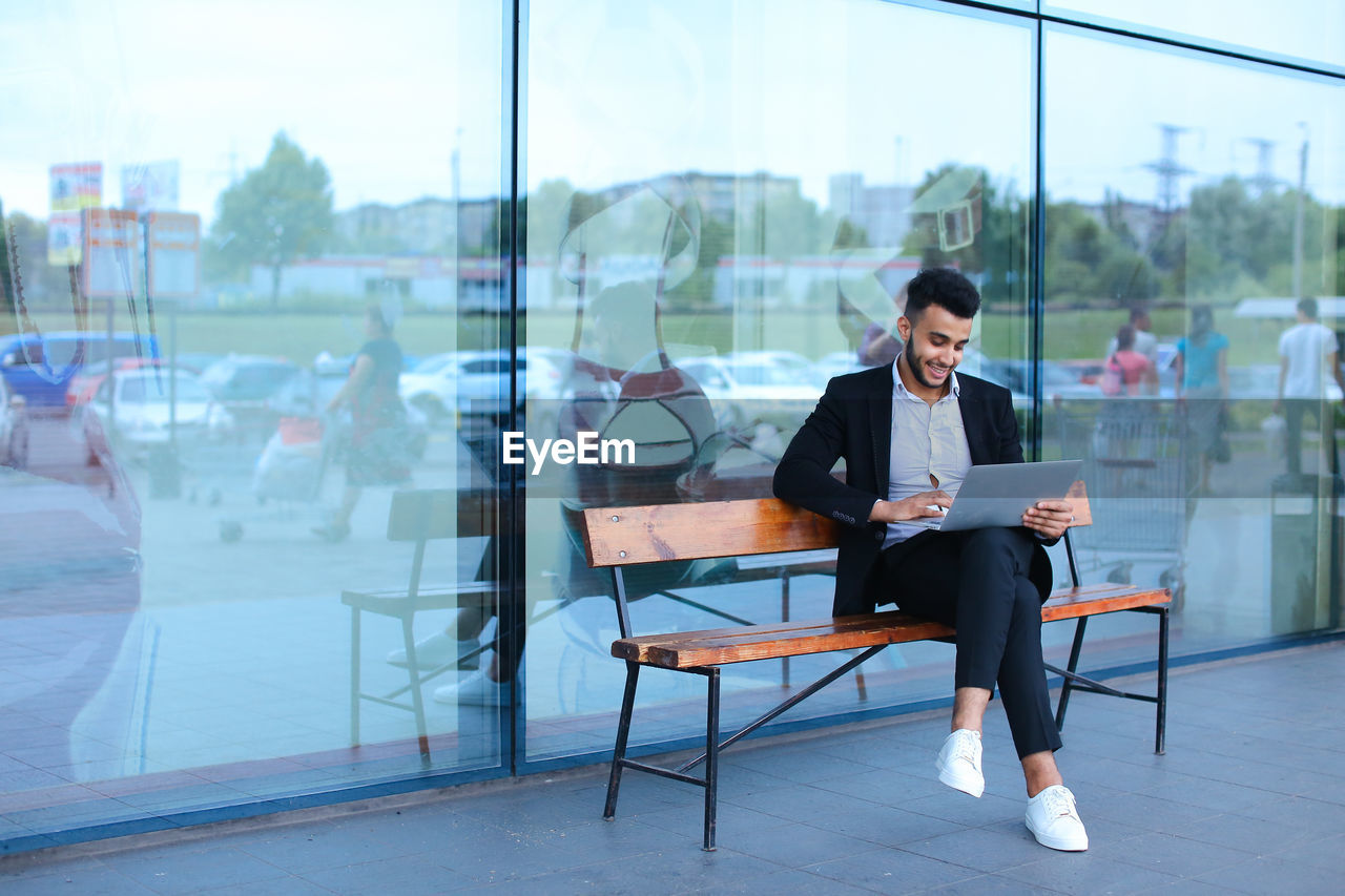 Businessman using digital tablet while sitting on bench outdoors