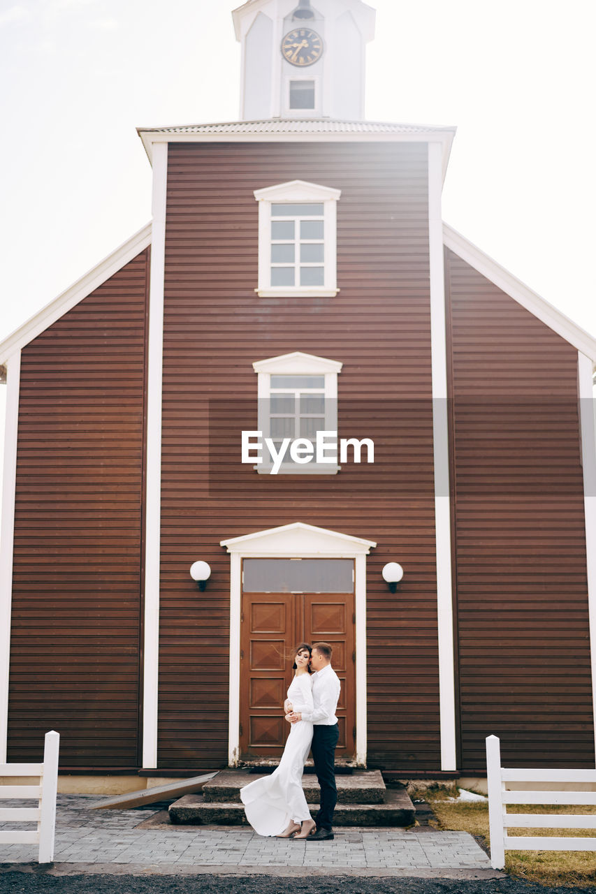 WOMAN STANDING OUTSIDE BUILDING AGAINST SKY