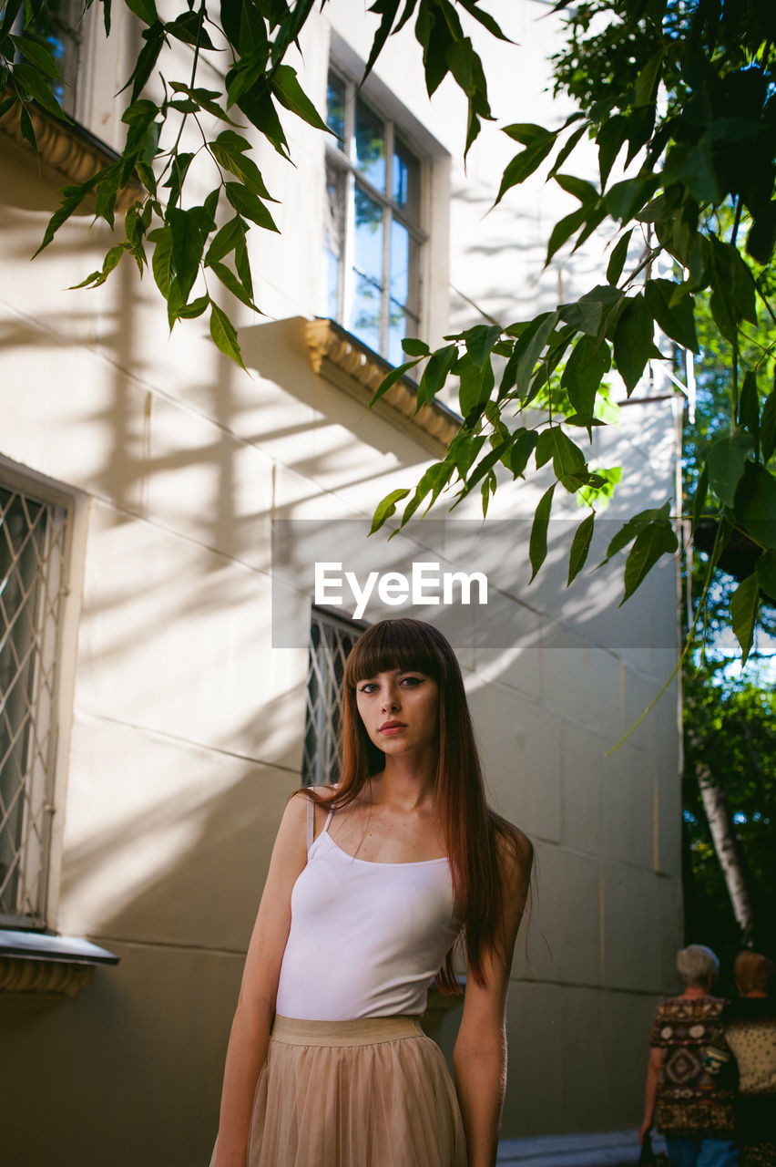 Portrait of young woman standing against building