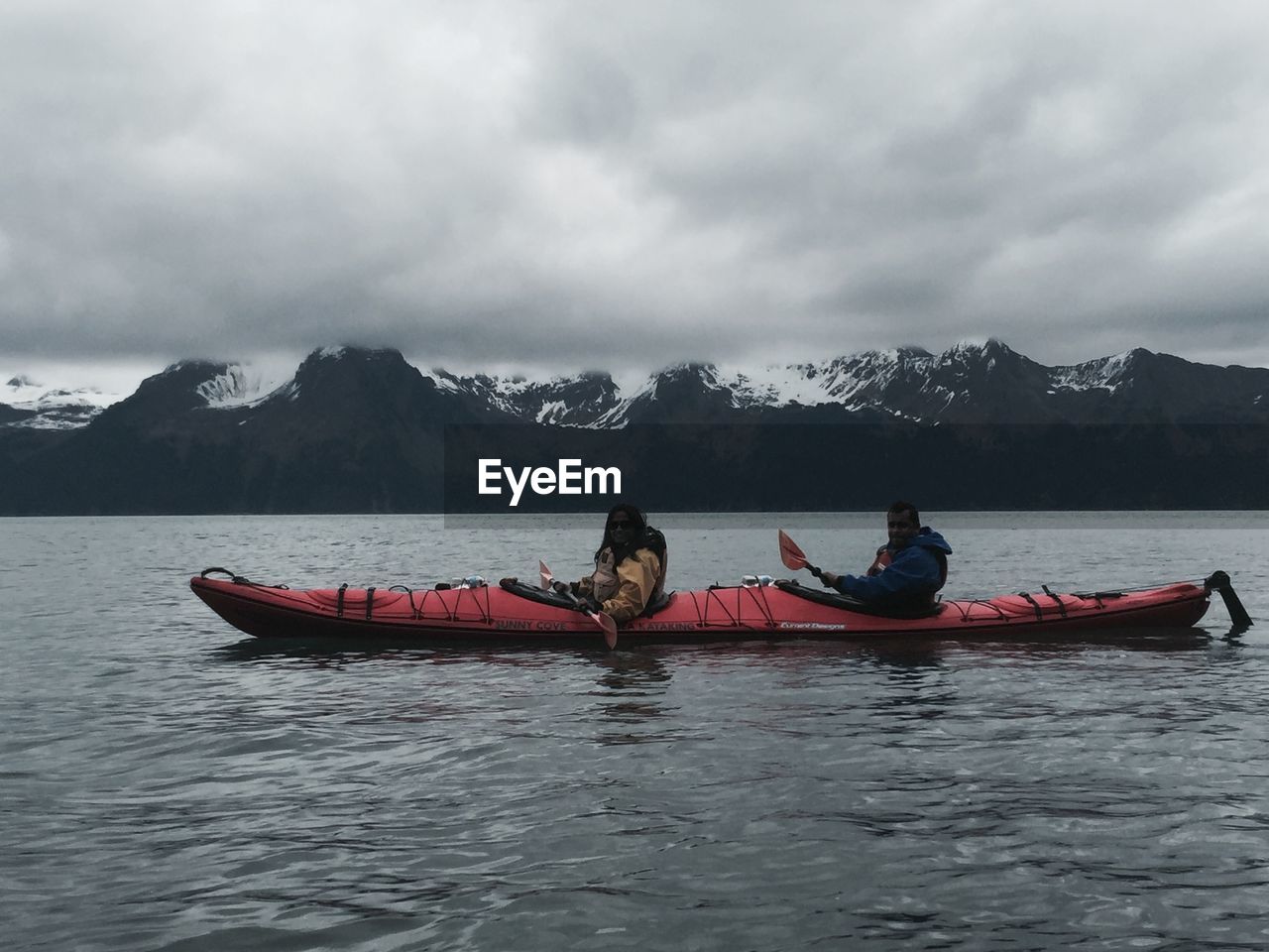 Hikers kayaking in lake against cloudy sky