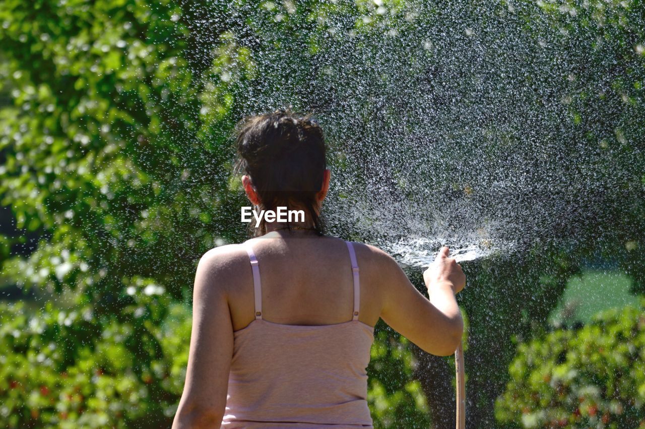 Rear view of woman spraying water in garden during sunny day