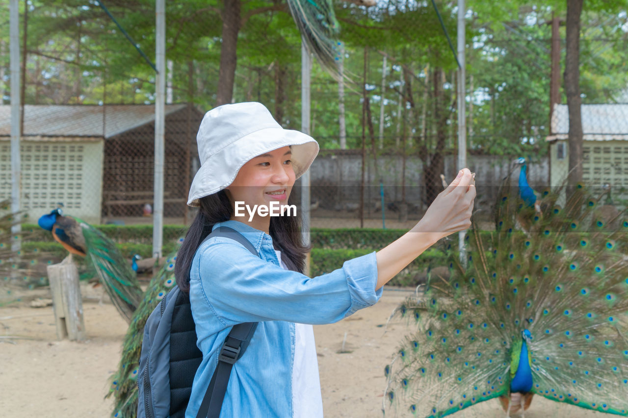 Smiling woman recording video against peacock