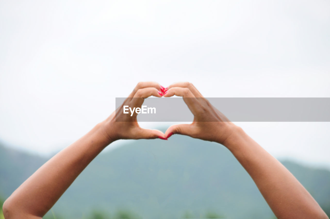 Cropped image of woman making heart shape from hands against sky