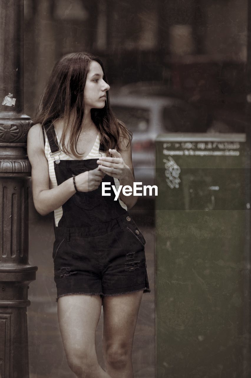 Teenage girl looking away while standing on footpath