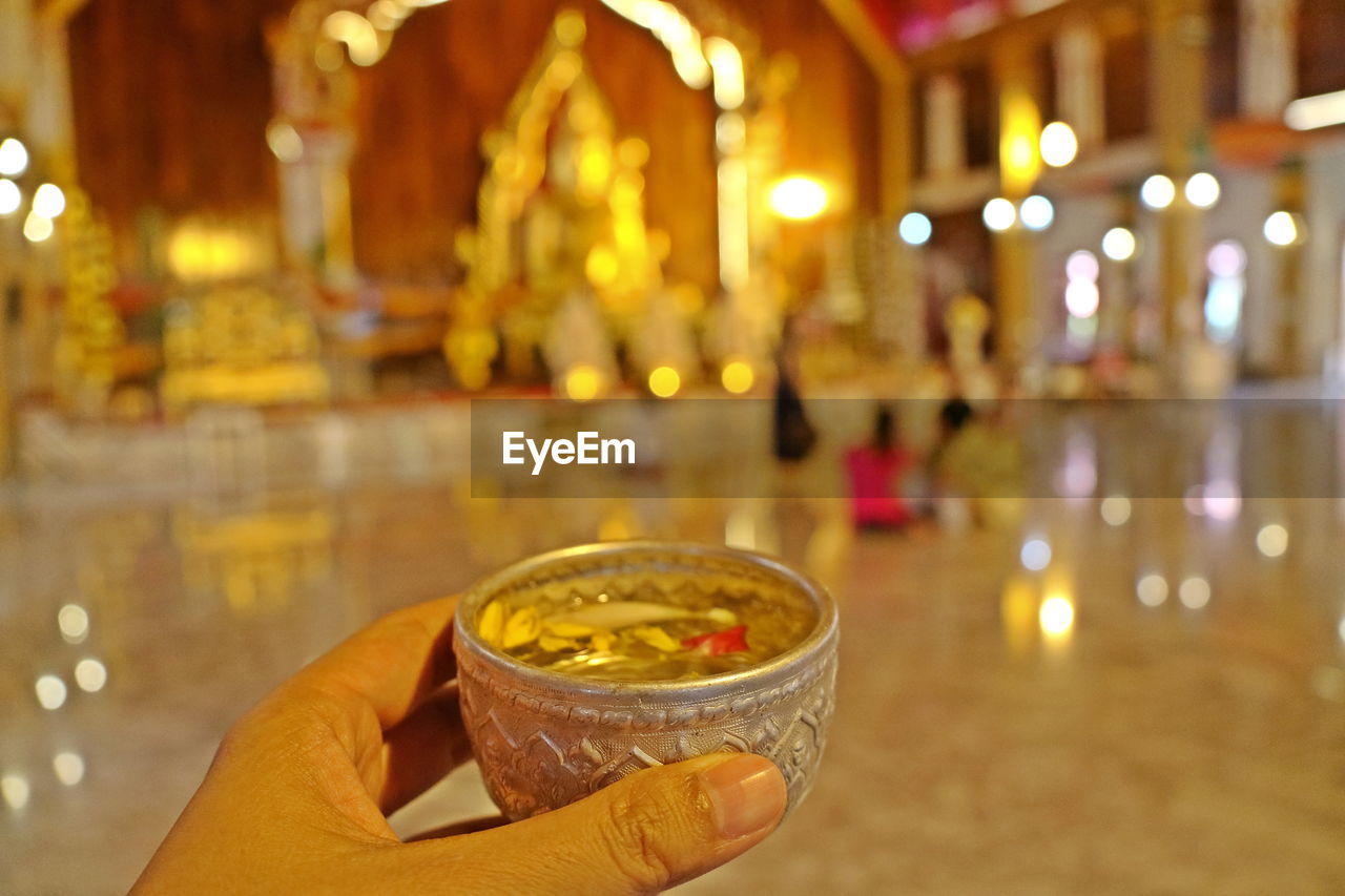 Hand holding bowl of scented water to sprinkle water onto a buddha image. songkran festival.