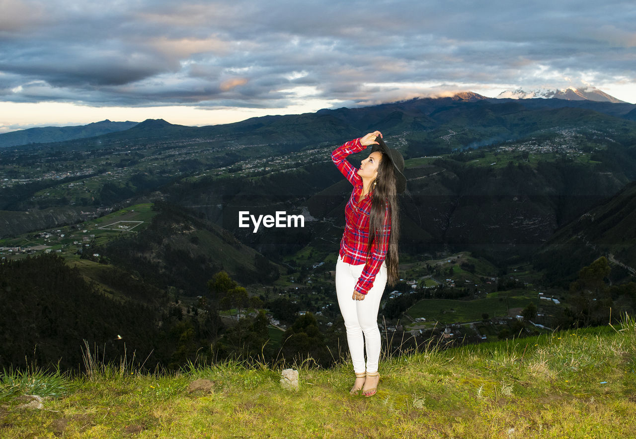 Woman standing on grassy field by mountains against cloudy sky