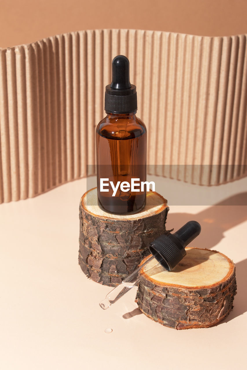 Glass dropper bottle with cosmetic serum on wooden stump podium with hard shadow. hyaluronic acid 