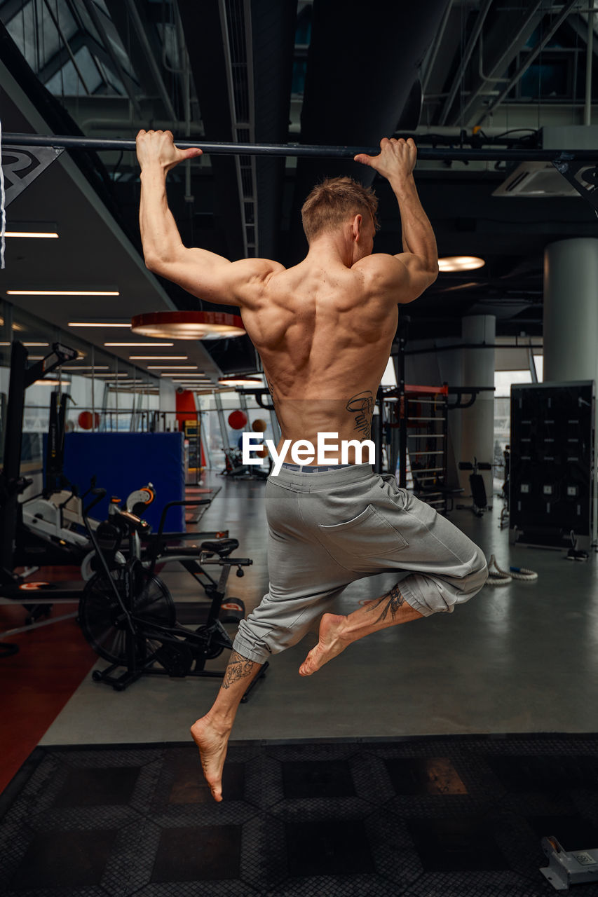 full length of shirtless man exercising in gym
