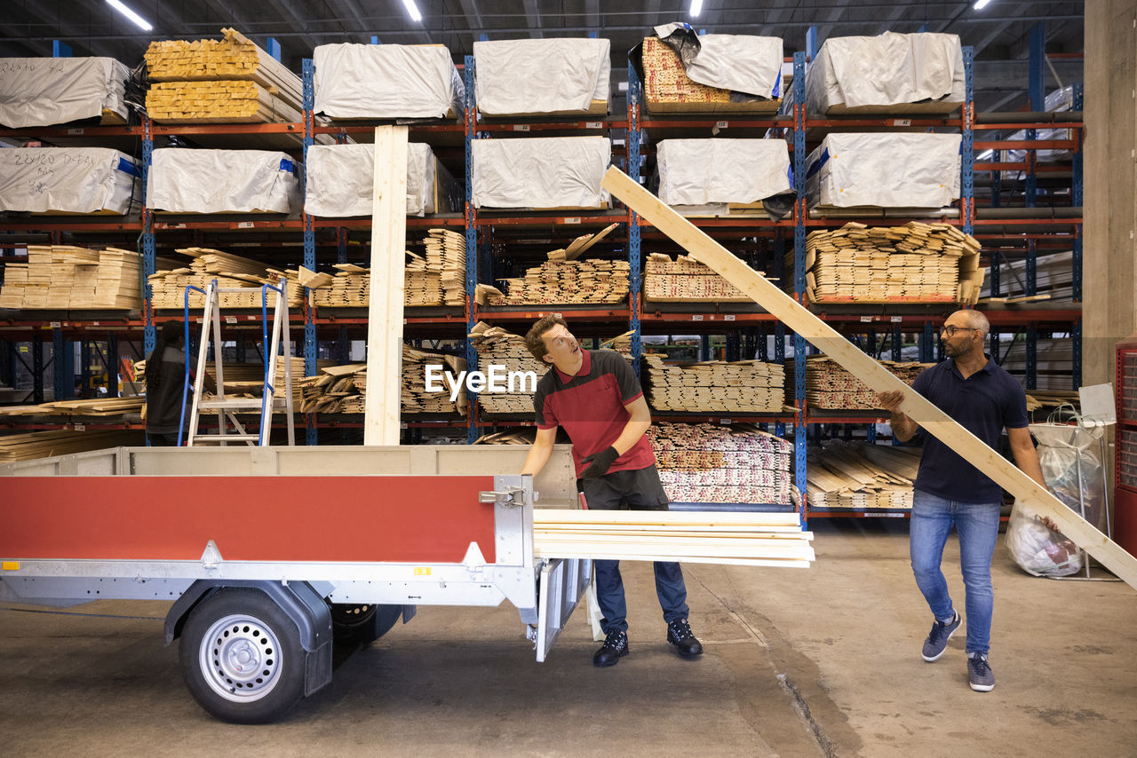 Male customer loading wooden plank in trailer at hardware store