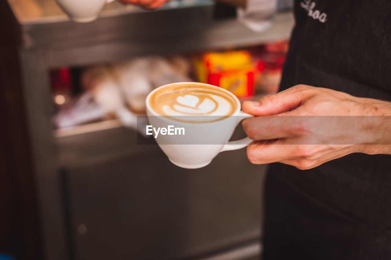 Midsection of barista holding coffee cup at cafe