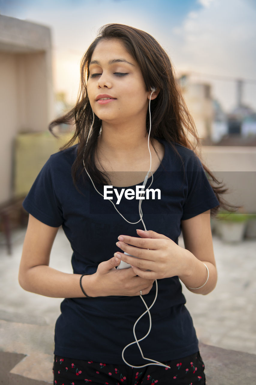 YOUNG WOMAN USING MOBILE PHONE WHILE STANDING ON CAMERA AT HOME