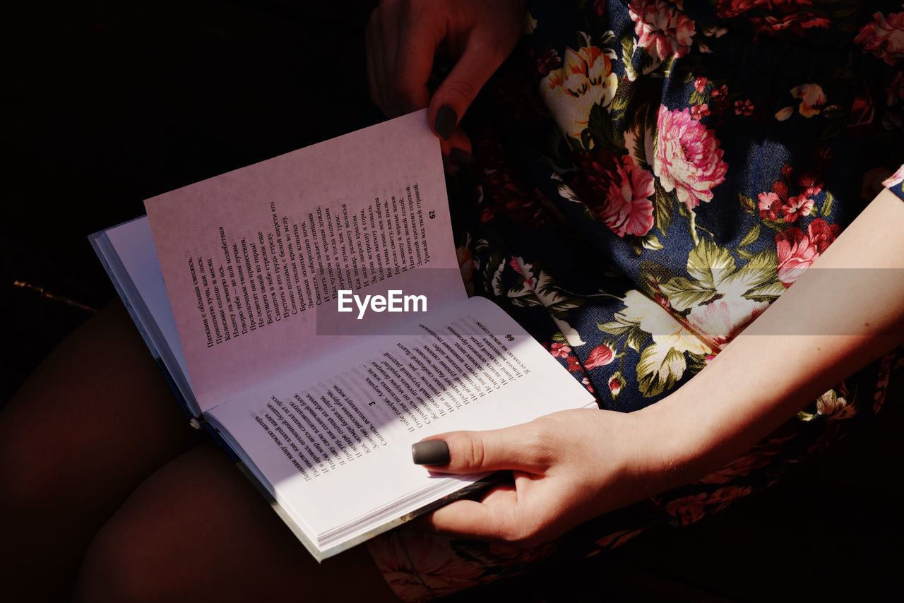 MIDSECTION OF WOMAN READING BOOK AT FLOWER