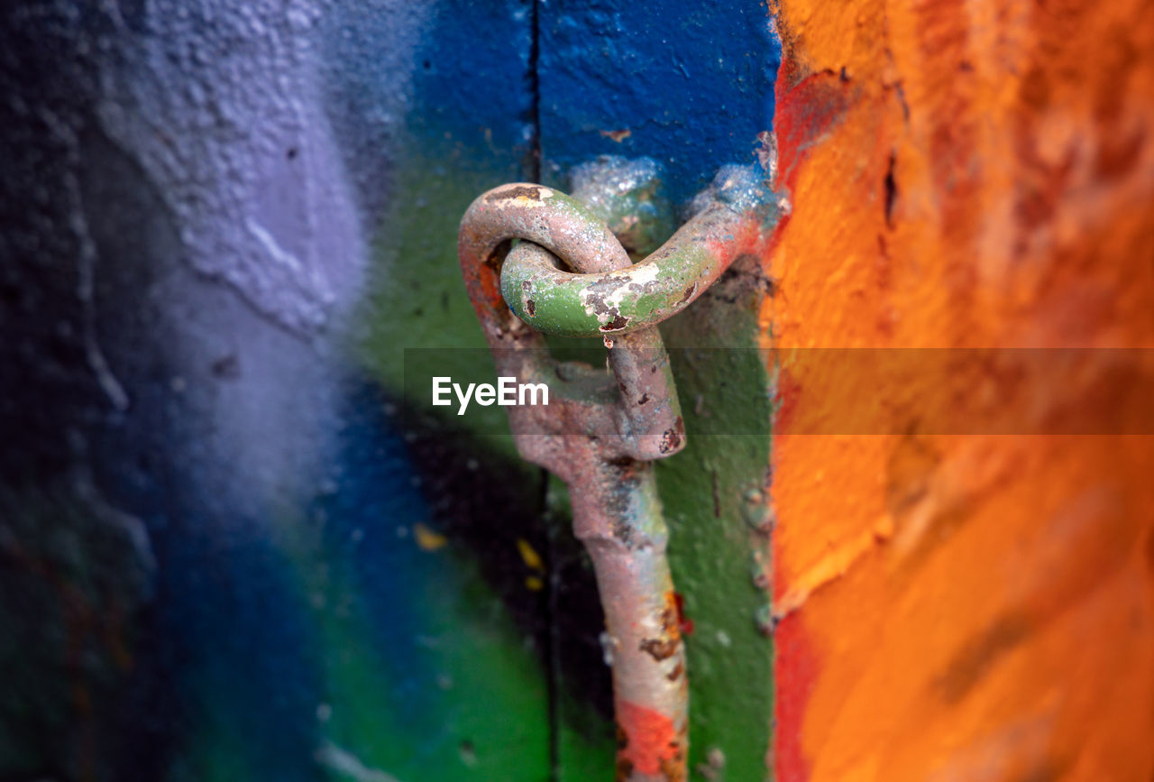 Close-up of rusty metal chain against colorful graffiti wall