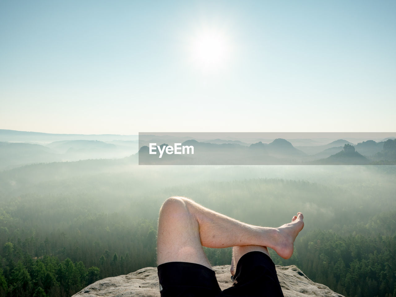 Barefoot male body in black pants sleeps on cliff. morning fog. natural park in sachsen, deutschland