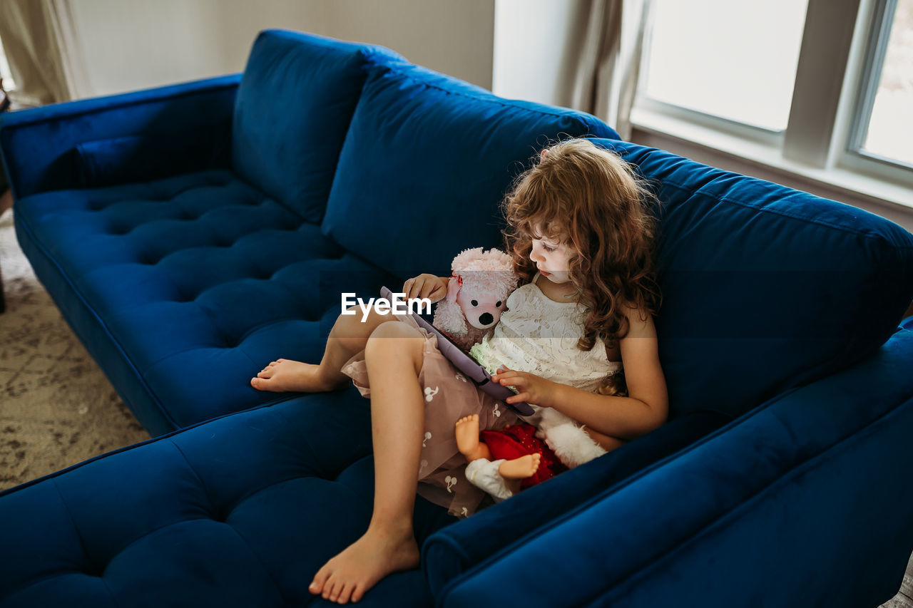 Young girl sitting inside on blue couch using tablet