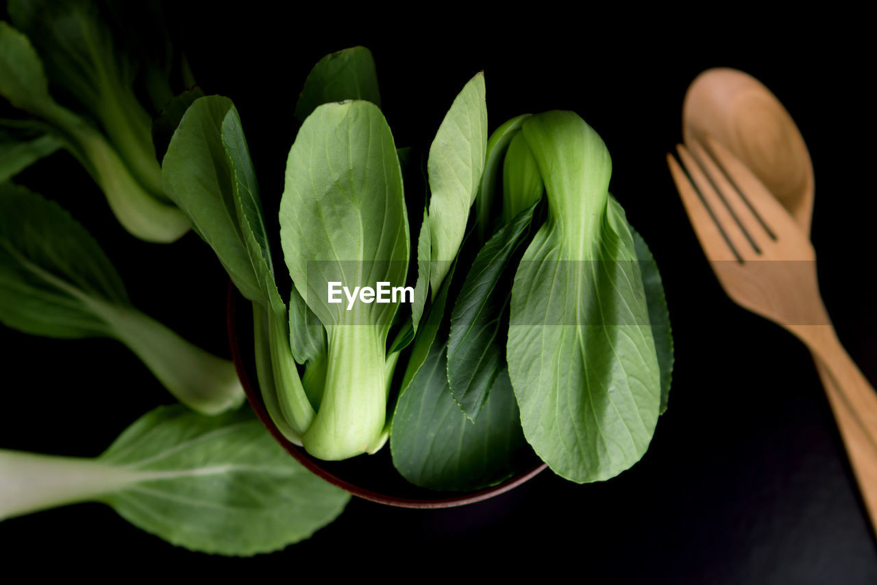 High angle view of leaf vegetables in bowl with wooden cutleries on black background