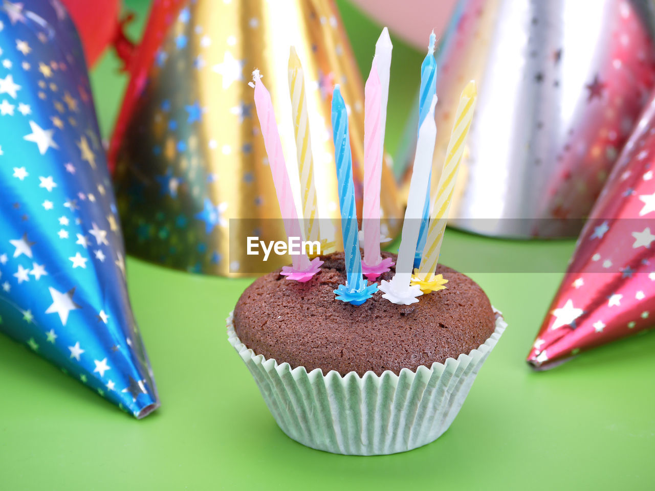 Chocolate muffin decorated with eight candles with party cone caps in the background