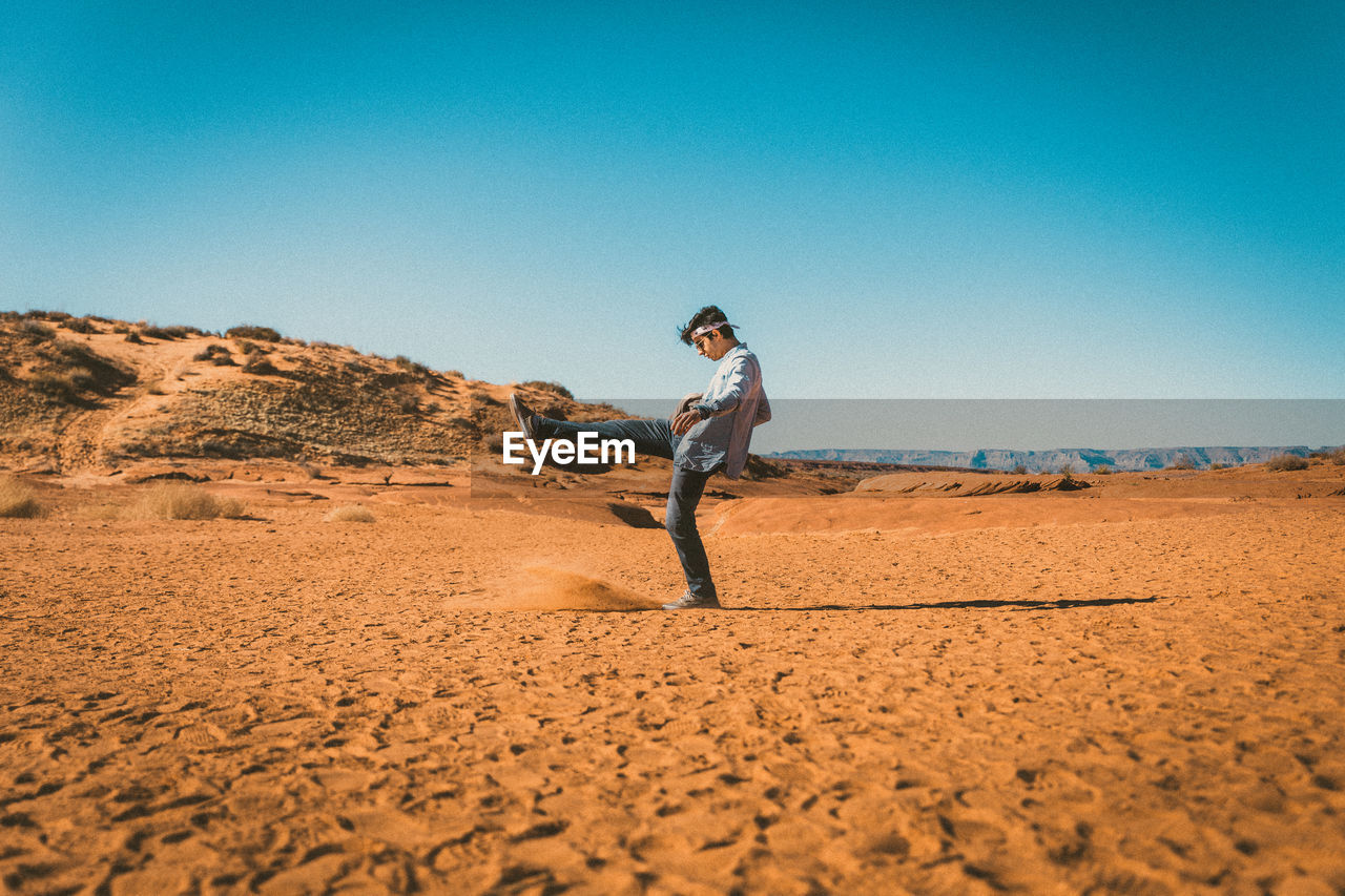 Side view of man kicking sand in desert