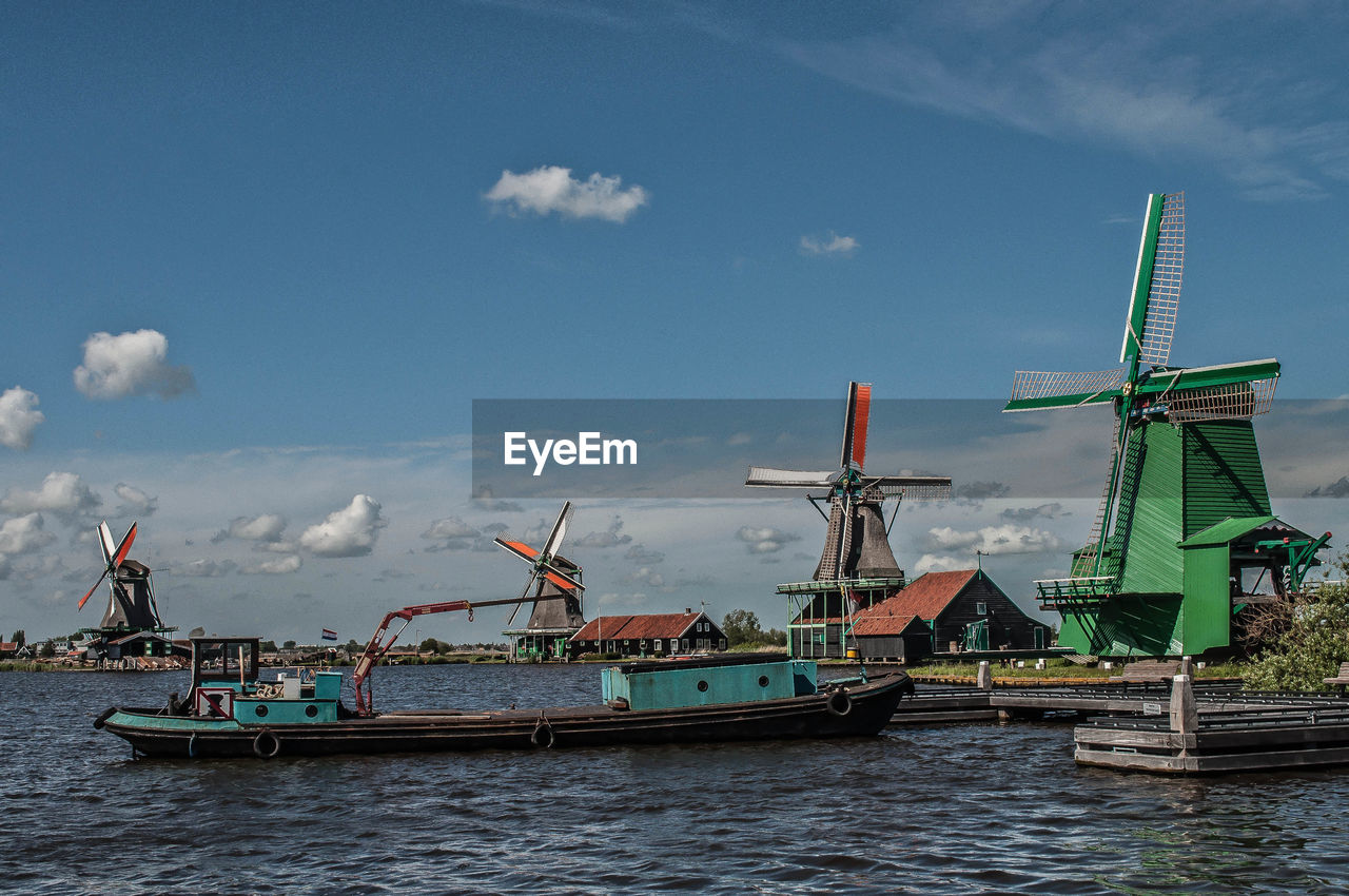 Boat moored in river by windmills against sky