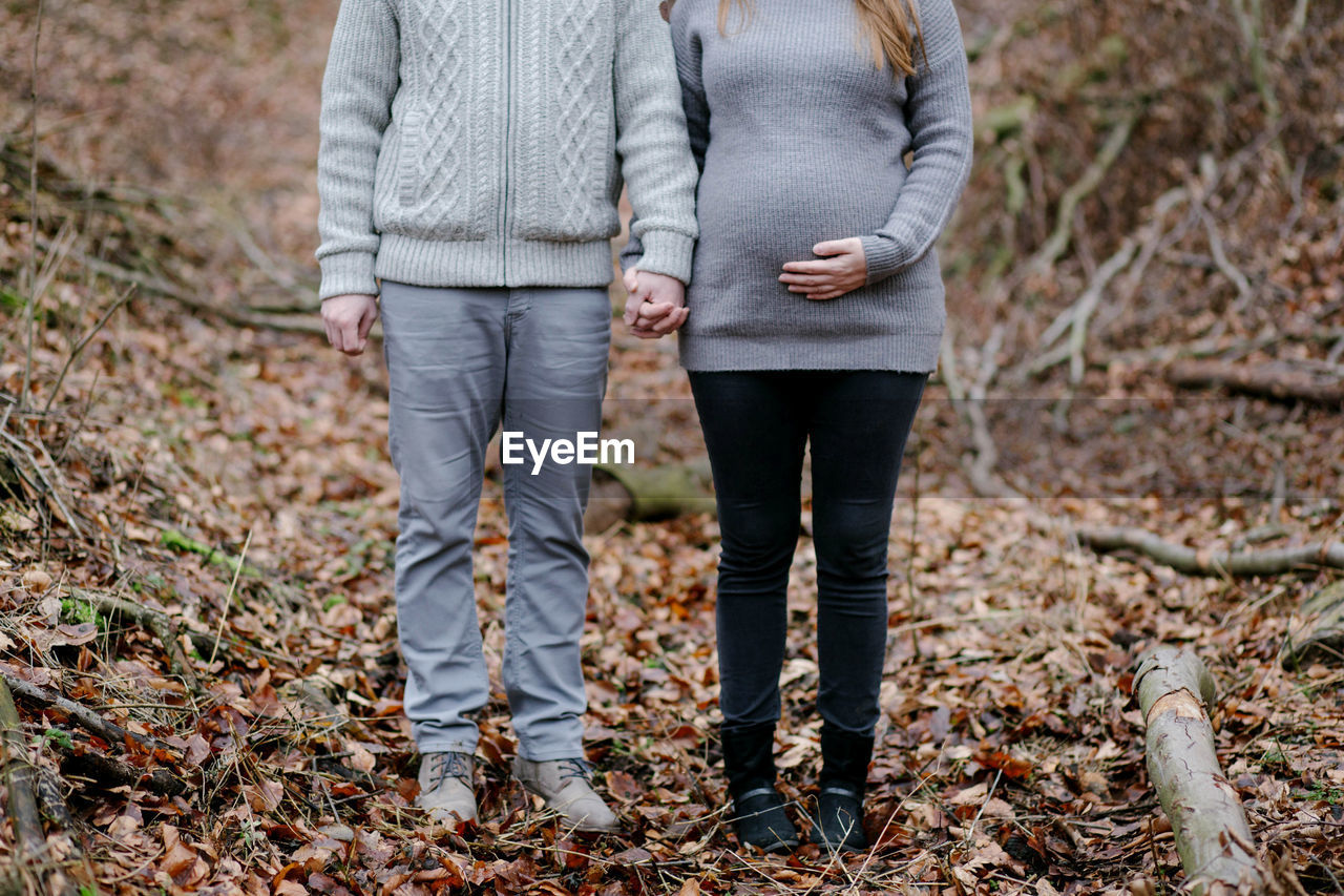 Low section of couple standing on autumn leaves in forest