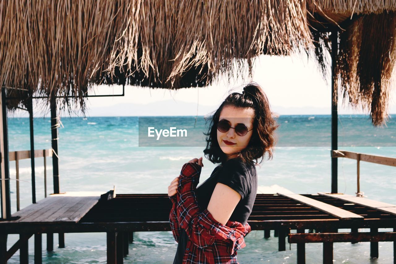 Portrait of smiling young woman standing in shed against sea at beach