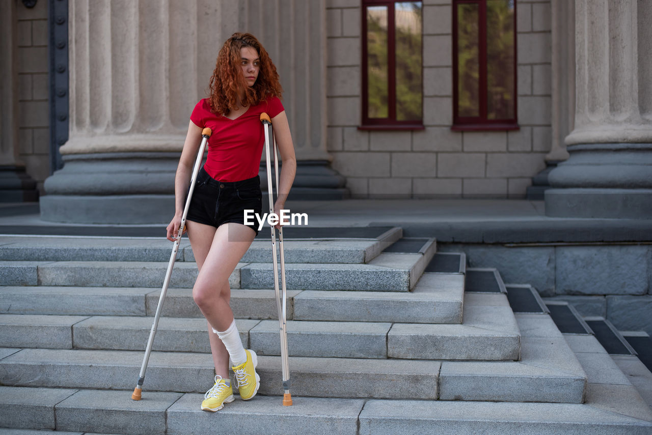 FULL LENGTH OF WOMAN LOOKING AWAY WHILE SITTING OUTDOORS