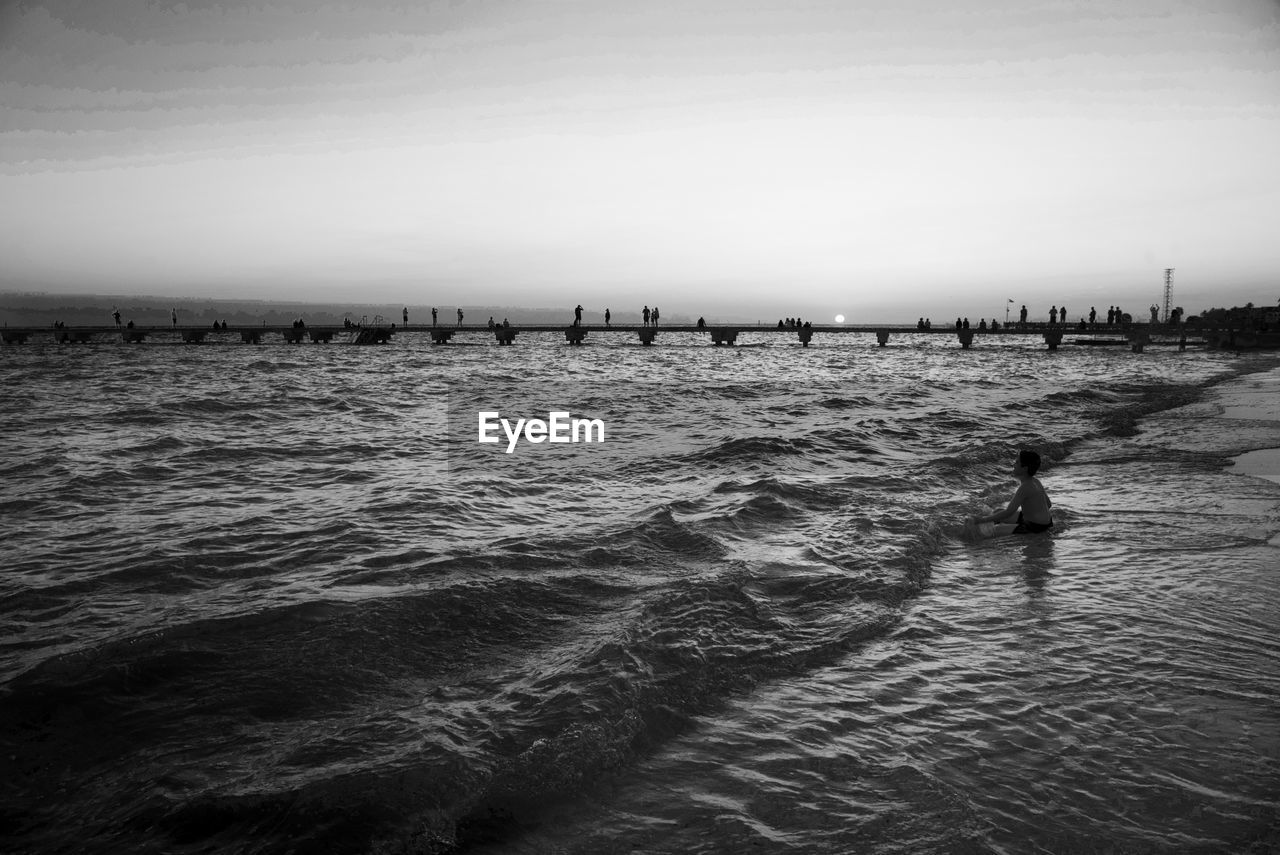 Boy sitting on shore at beach during sunset