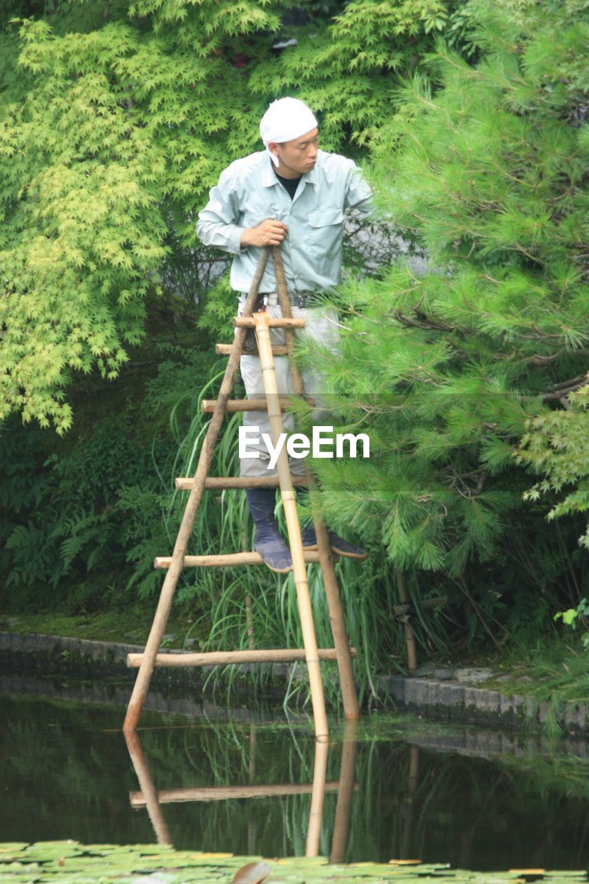 MAN STANDING BY TREE IN GARDEN