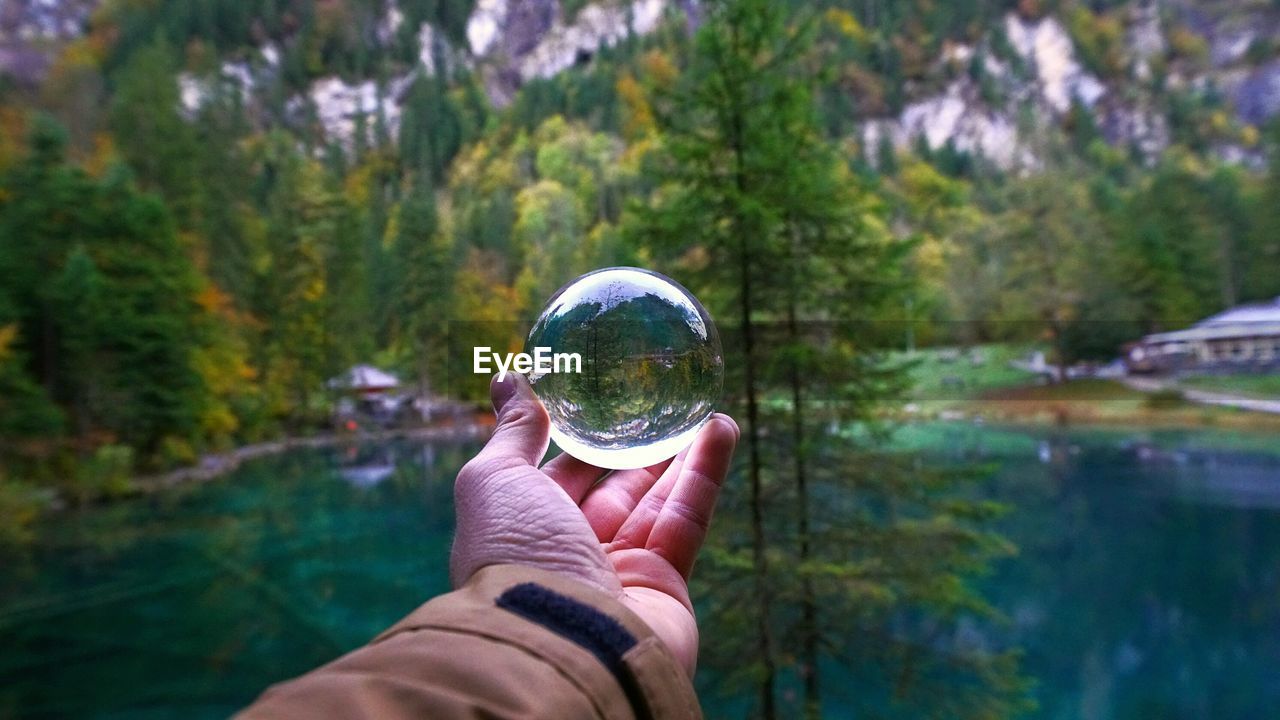Cropped hand of man holding crystal ball by lake