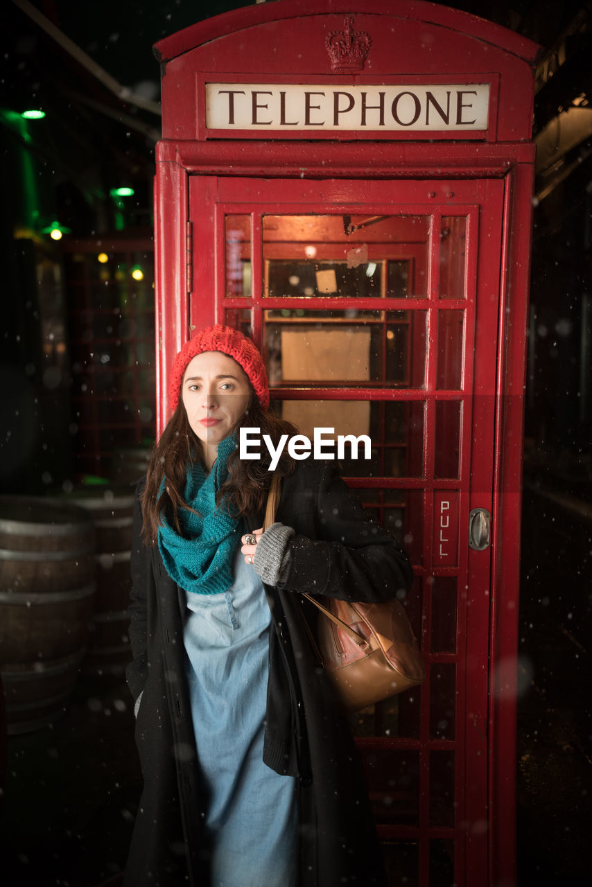 Portrait of woman standing against telephone booth